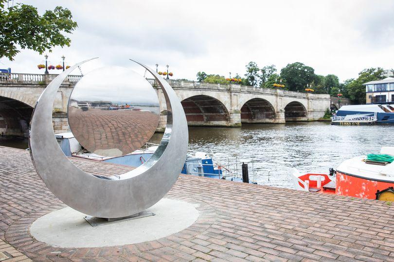 A large crescent moon shaped metallic sculpture next to the thames