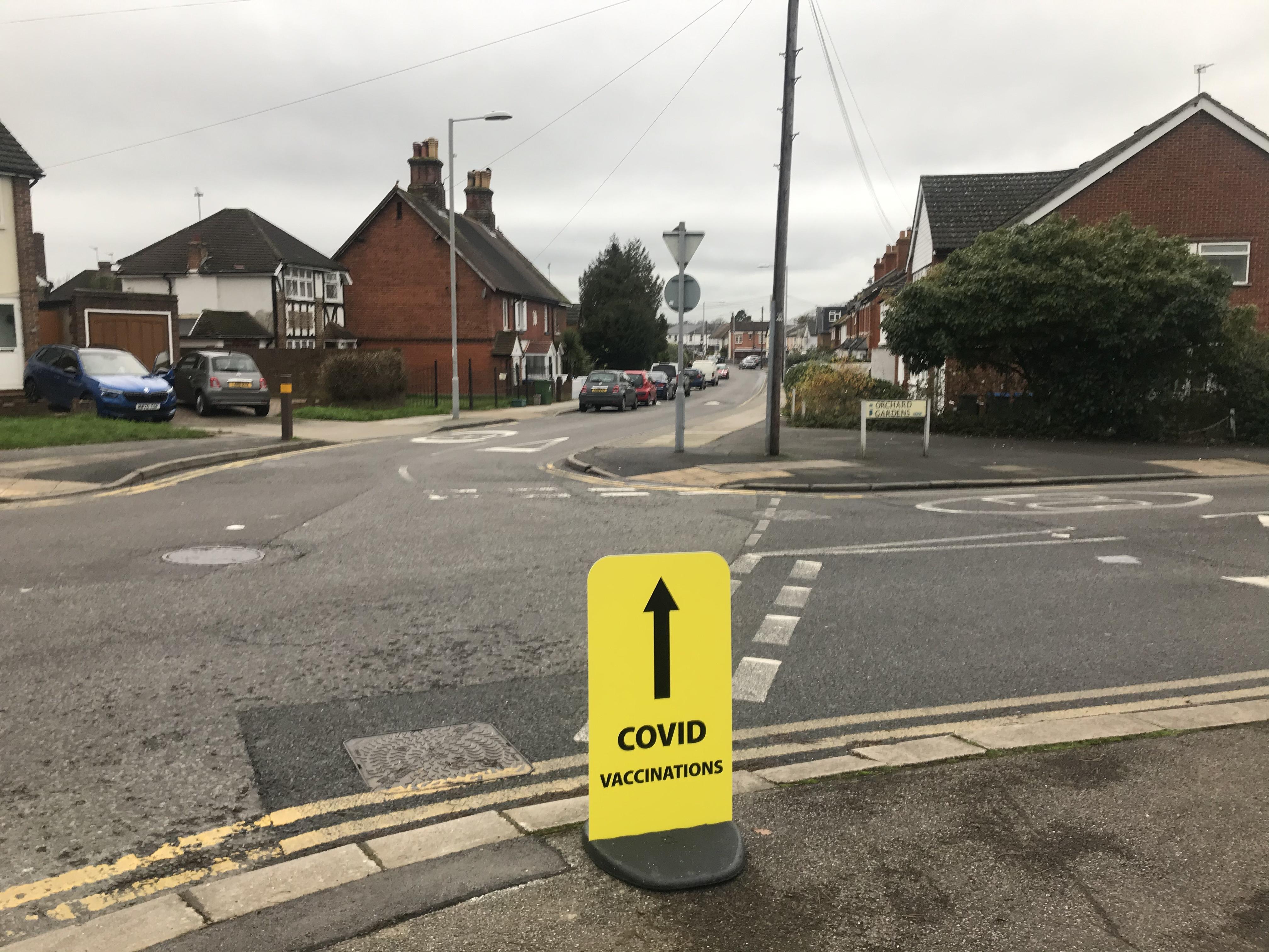 A bright yellow sign directing people to a vaccination centre in the middle of an empty residential street.