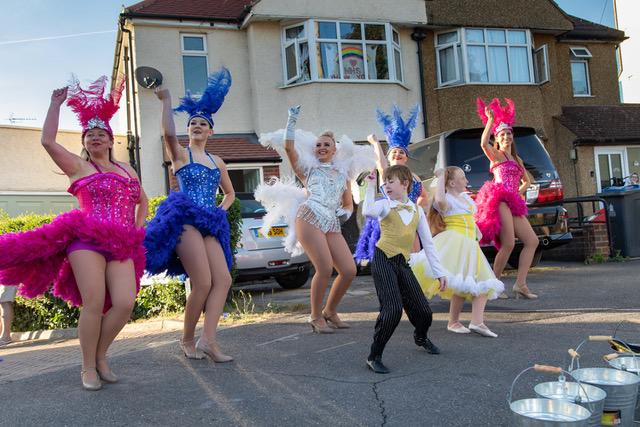 A family in carnival style dance costumes dance together outside of their house