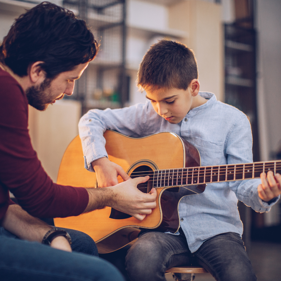 A male teacher teaches a young boy to play guitar