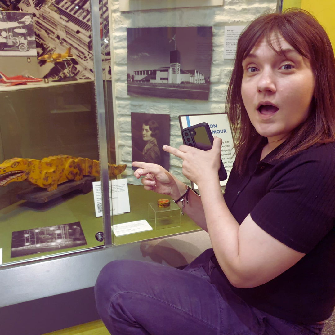 Woman pointing to something behind museum display glass with mouth open in surprise.