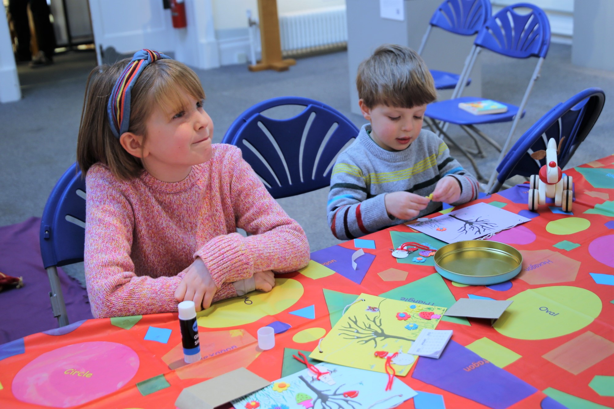 Picture of a little girl, and boy at a craft table, cutting out shapes and gluing them to paper