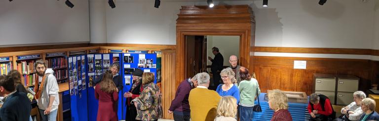 People chatting in groups in a wood-panelled room lined with bookshelves